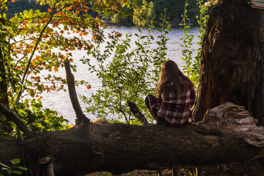 Woman sitting on a log by a lake in the woods